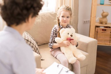 Koltuk otururken teddybear ile sevimli sarışın çocuk öğretmen veya anne bakıyor