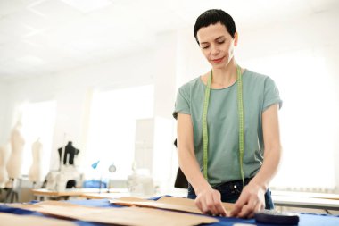 İş yerinde ayakta iken kesme önce kumaş parçası üzerinde kağıt desen kadar sabitleme olgun esmer kadın terzi