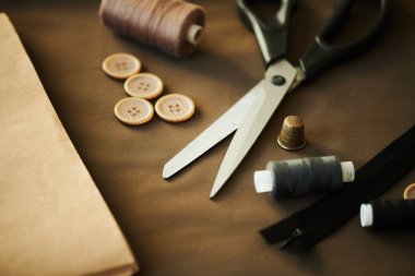 Çeşitli düğmeler, makas, renkli iplik makaraları, fermuar ve terzi işyerinde kahverengi tekstil üzerinde yüksük