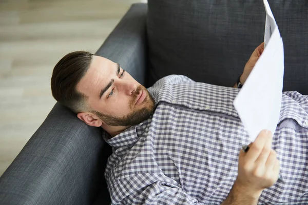 Seriózní Mladý Makléř Přesnoji Relaxaci Pohovce Domácí Kanceláři Čtení Finančních — Stock fotografie