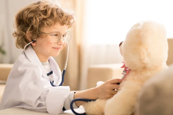 可爱的金发小男孩卷发检查柔软的白色泰迪熊与听诊器 而在家里或幼儿园玩 — 图库照片