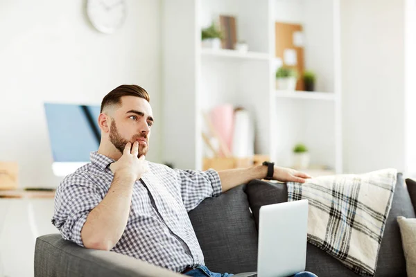 Jonge Pensive Man Met Laptop Zijn Knieën Zittend Sofa Proberen — Stockfoto