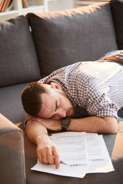 疲惫的年轻家庭办公室经理躺在沙发上 在处理财务文件后睡觉 — 图库照片