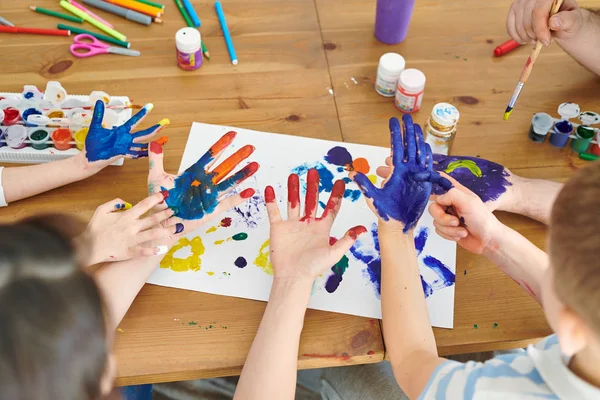 若い女性と彼女の子供たちは 紙にプリントを作るためにグアッシュで手のひらを描きます — ストック写真