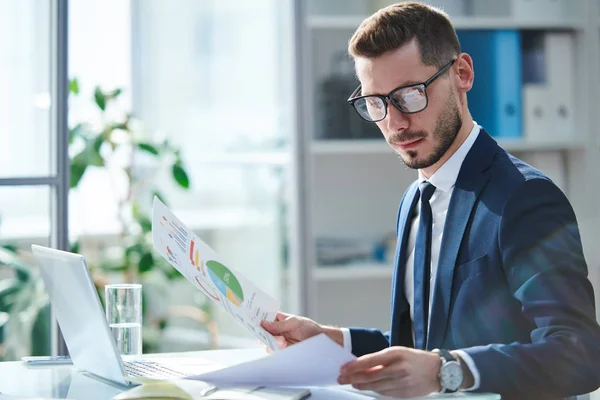 Grave Giovane Economista Occhiali Abbigliamento Formale Guardando Attraverso Documenti Finanziari — Foto Stock