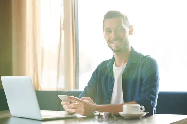 Jonge Vrolijke Zakenman Met Smartphone Zittend Tafel Voor Laptop Sms — Stockfoto