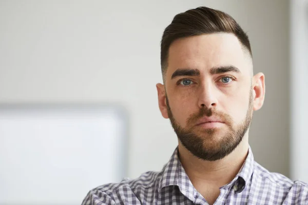 Calm young bearded man with relaxed expression looking at you while standing in front of camera