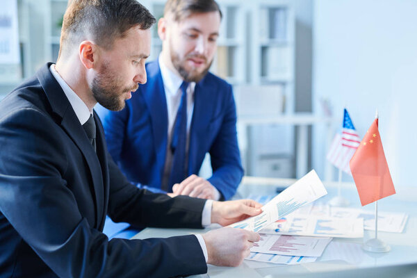 Небольшая группа бизнесменов читает деловые документы во время подготовки доклада или вопросов к конференции
