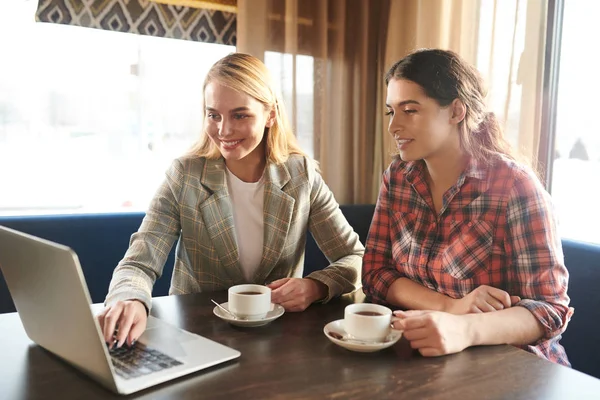 Dos Jóvenes Empresarias Con Tazas Sentadas Junto Mesa Frente Laptop —  Fotos de Stock