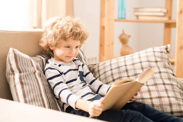 可爱和聪明的小男孩穿着休闲装坐在舒适的扶手椅和阅读故事书 — 图库照片