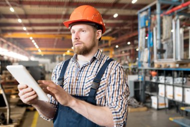 Young confident factory engineer using touchpad while surfing in the net for technical characteristics of new industrial equipment