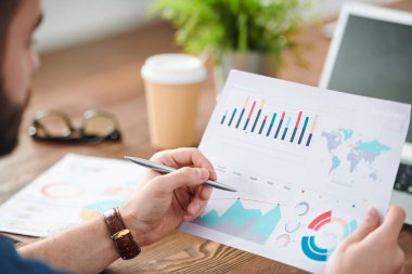 Finansal bilgileri analiz ederken belge nin grafiğini kalemle işaret eden genç ekonomist veya analist