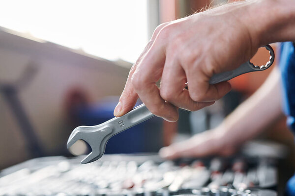 Hand of young technician or repairman with metallic wrench during working process or technical check-up of car