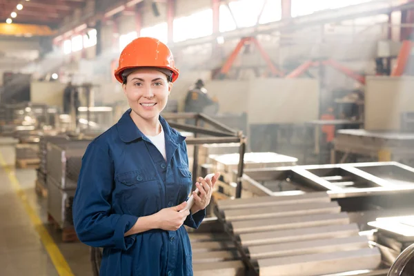 自信的女工程师在工厂工作时使用小工具 穿着蓝色工作服和橙色防护头盔 — 图库照片
