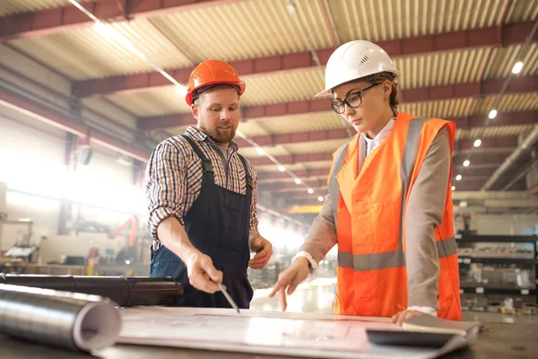 Két Fiatal Mérnök Sisakokban Egyenruhában Ipari Részletek Tervrajzán Munkaértekezleten — Stock Fotó