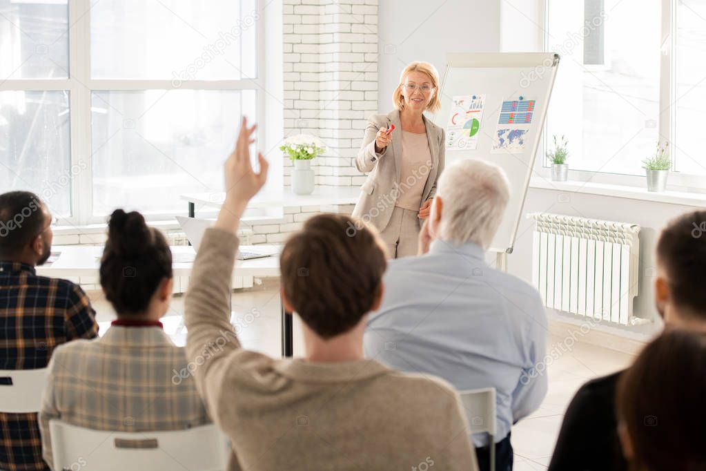 Elegant teacher pointing at one of students at lesson after asking question about the lecture