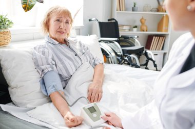 Tedavi bölümünde hasta yaşlı kadın hasta yatakta oturan ve doktor onun kan basıncını ölçme dinleme