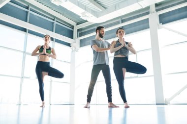 Aktif giyim erkek eğitmen eğitim sırasında onun yanında dururken yoga egzersiz ifit kızlardan biri yardım