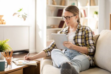 Evde proje üzerinde çalışırken rahat kanepede oturan ve günlük notlar yapma gözlük İçerik yaratıcı öğrenci kız