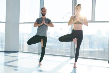 Young active couple keeping balance while standing on one leg with their hands put together by chest