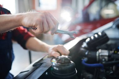 Çalışma sürecinde otomobilin açık motoru üzerinde anahtar tutan genç tamircinin eli