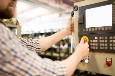 Atölyede kontrol panelinin önünde duran ve endüstriyel makinenin duvarında sergilenen ve kırmızı düğmeye basan çağdaş teknisyen