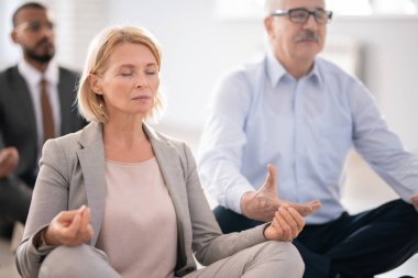Takım elbiseli yaşlı sarışın kadın ve iş arkadaşları nilüfer pozotururken mola meditasyon