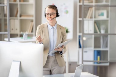 İçerik kendinden emin genç kadın webinar öğretmen kulaklık ve gözlük bilgisayar önünde duran ve sunum online tutarken el gesturing, video konferans konsepti