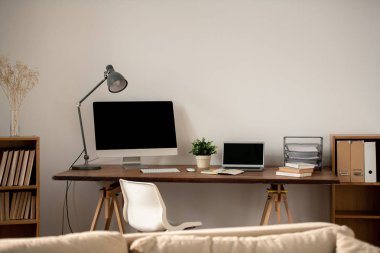 Workplace of freelancer or home office employee with table against wall and number of supplies and gadgets for work