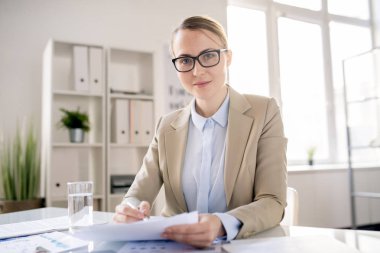 Gözlüklü içerik çekici genç ofis uzmanı portresi masada oturan ve rapor ile çalışan