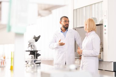 Laboratuvarda bilimsel proje yi tartışan laboratuvar önlüklerinde ciddi deneyimli tıbbi araştırmacılar, Arap adam meslektaşına fikrini açıklıyor