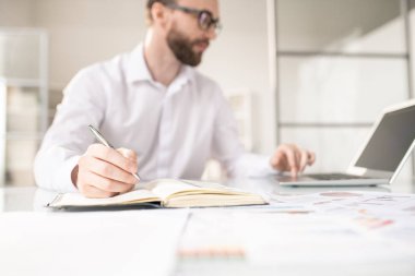 Çağdaş erkek komisyoncu işyeri tarafından çalışma notları yaparken defter sayfası üzerinde kalem ile elini tutarak