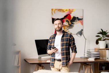 Kamera önünde işyerinin arka planda duran elinde akıllı telefon ile Casual ev ofis çalışanı
