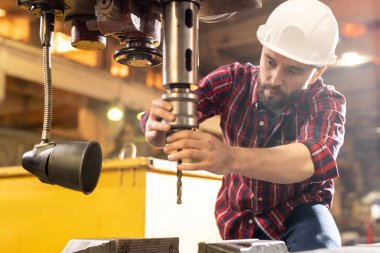Young engineer or machinebuilder checking large industrial drill before using it in processing work