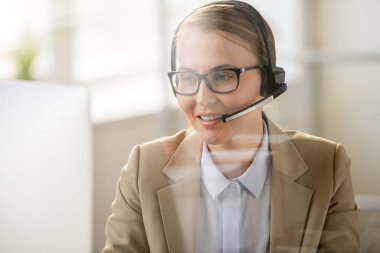 İçerik gözlük güzel genç iş kadını müşteri konuşurken hands-free cihazı kullanarak, o programlama şirketinin çağrı merkezinde çalışıyor