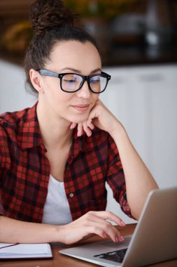 Net yeni fikirler için sörf yaparken gözlük ve casualwear pretty genç esmer tasarımcı dizüstü ekran bakarak