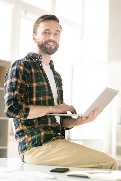 Jovem Barbudo Feliz Casualwear Usando Laptop Enquanto Sentado Mesa Frente — Fotografia de Stock