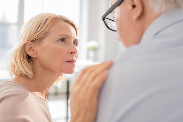 Пожилая блондинка, поддерживающая женщину, прикасаясь к плечу своего пациента или соседа по группе, слушая его историю
