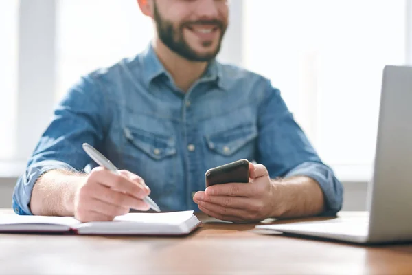 机で仕事を計画しながら ノートのページの上にペンで手をつないでいるデニムシャツの現代の若いビジネスマン — ストック写真