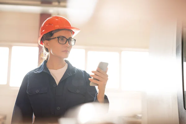 Jovem Engenheira Uniforme Protetora Capacete Leitura Dados Gadget Enquanto Olha — Fotografia de Stock