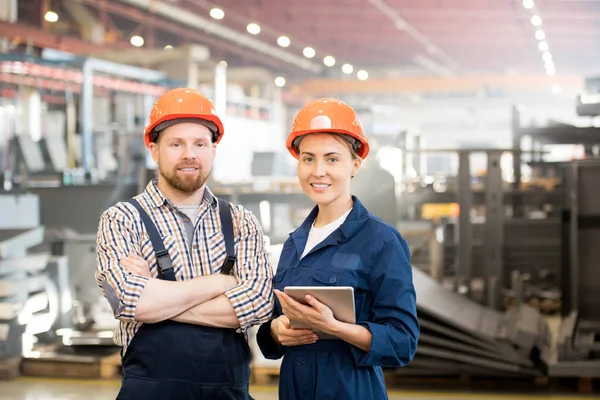 两名年轻的当代技术人员穿着工作服和防护头盔在工厂集体工作 — 图库照片