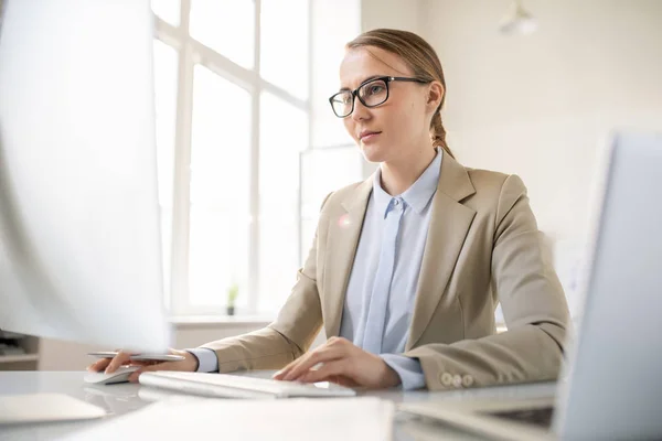 メガネで忙しい若い女性オフィスマネージャーがテーブルに座り データを分析しながらコンピュータを使う — ストック写真