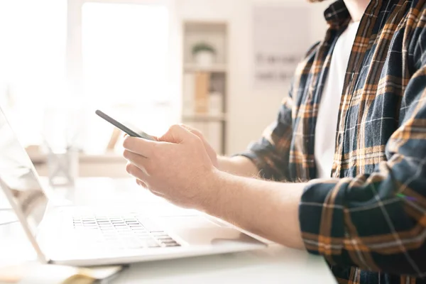 Junger Mann Freizeitkleidung Hält Smartphone Über Laptop Auf Schreibtisch Während — Stockfoto