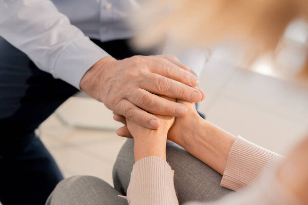 Aged man holding hands of upset mature female while taking care of her problem and supporting her
