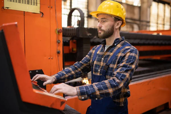 年轻的当代工程师 身穿制服 头戴硬帽 站在终端旁 控制着工业机器 — 图库照片