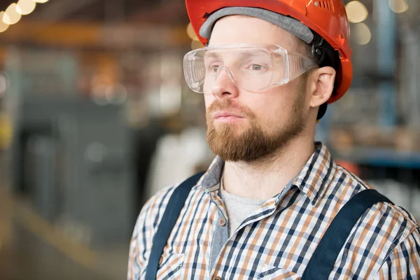 Modern fabrika veya sanayi fabrikasının sakallı genç mühendisi kamera önünde atölyede duruyor