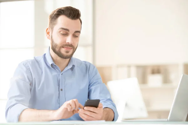 オフィスに座っている間にメッセージ通信のために彼のスマートフォンを使用して 現代の若いオフィスマネージャー — ストック写真