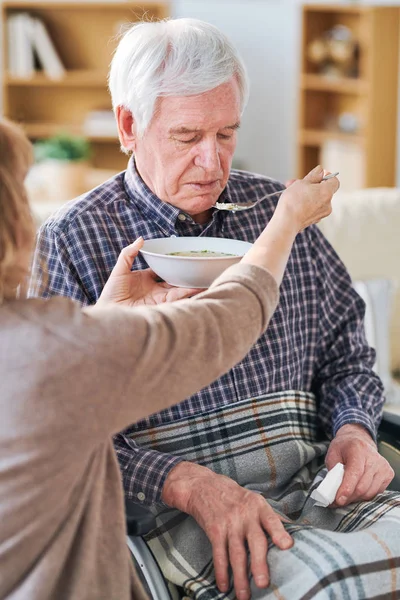老年女性拿着勺子和盘子与汤由她的残疾病人或丈夫的嘴 而喂他晚餐 — 图库照片
