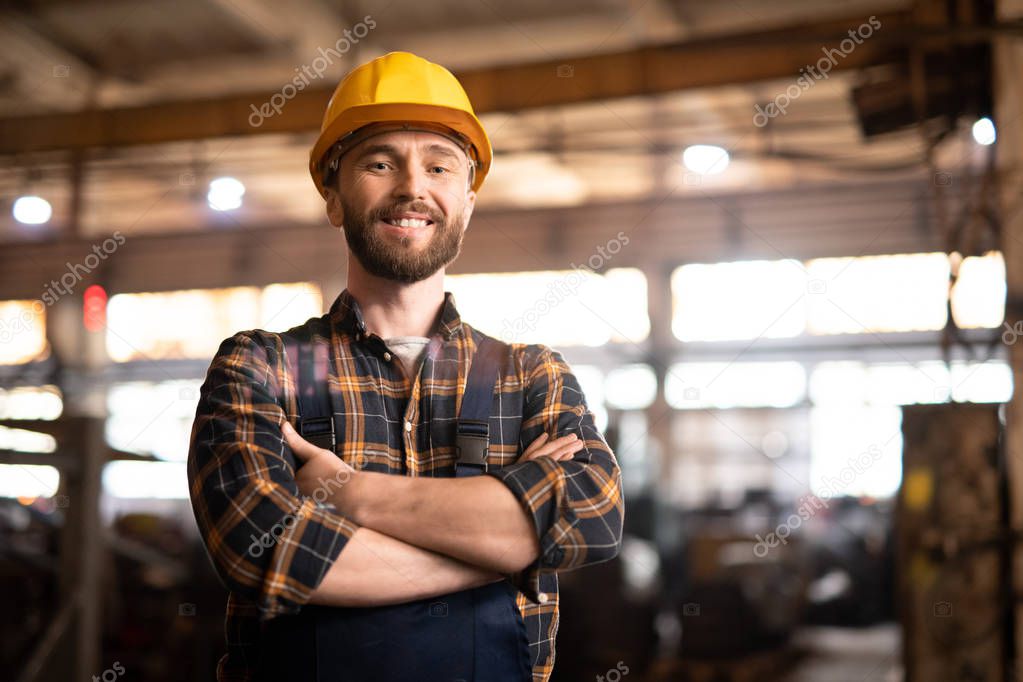 Young attractive bearded repair service technician or engineer of heavy industry factory smiling at you