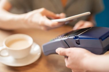 Kafe veya restoranda temassız ödeme işlemi sırasında elektronik makine üzerinde akıllı telefon tutan çağdaş kişi